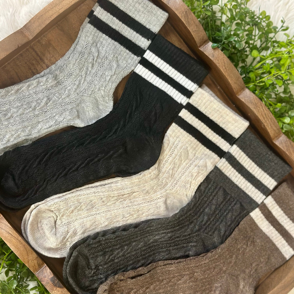Set of four socks in gray, black, and brown with striped patterns on a wooden surface.