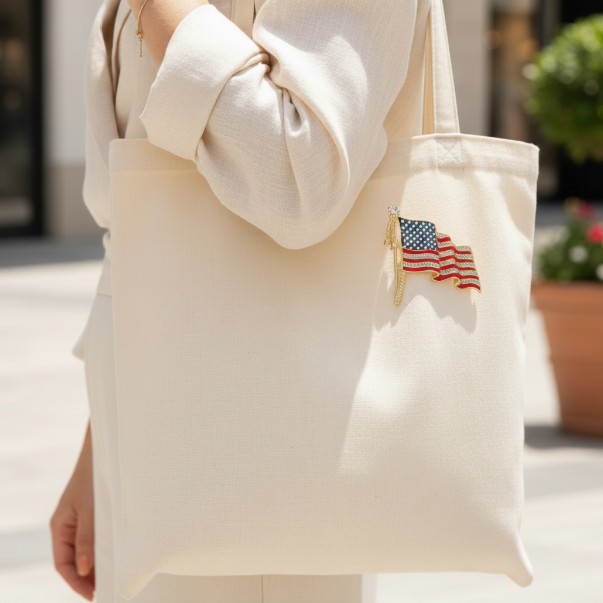 Person holding a beige tote bag with an American flag design outdoors.