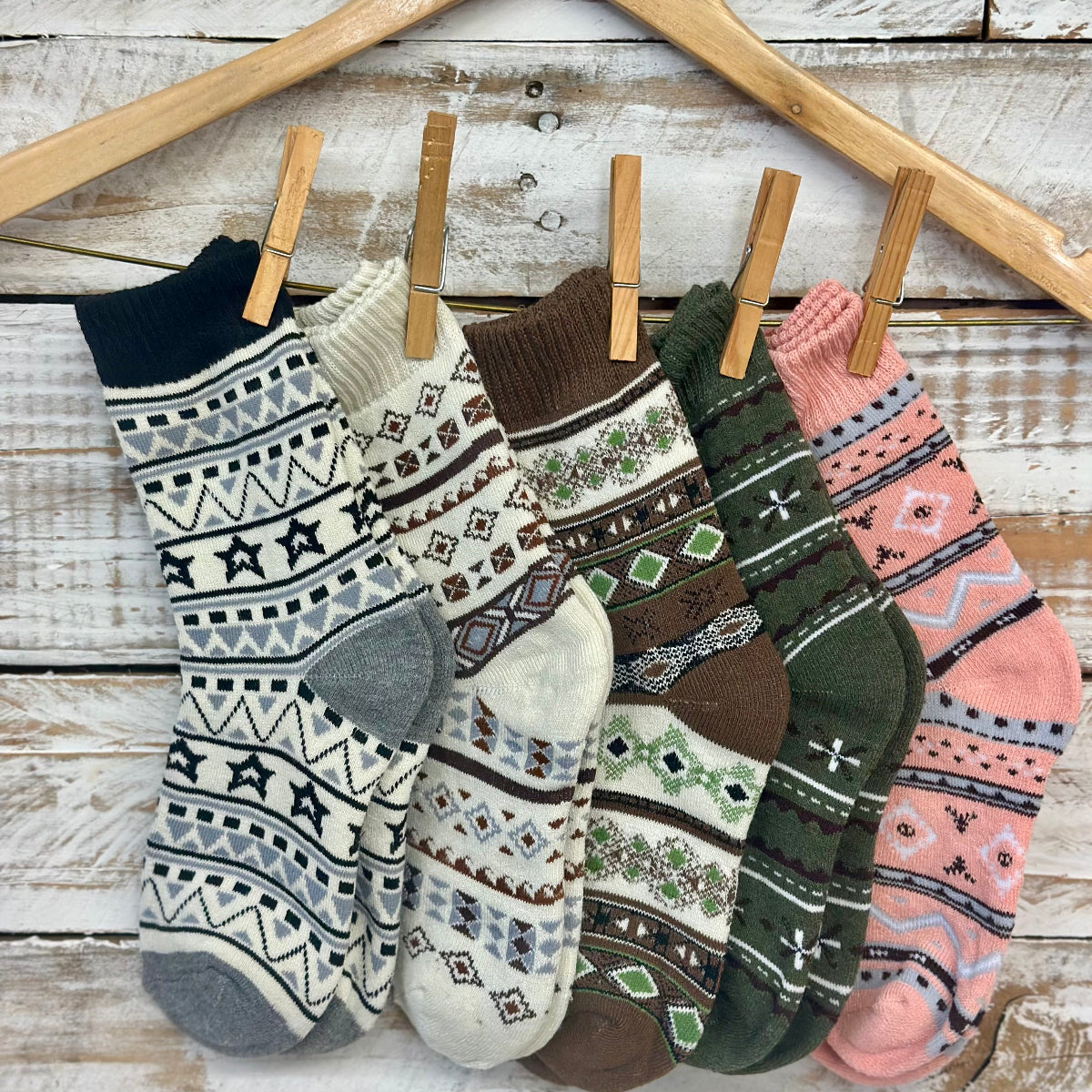 Five pairs of patterned socks hanging on a wooden rack with clothespins against a rustic wooden background. Catherine cole