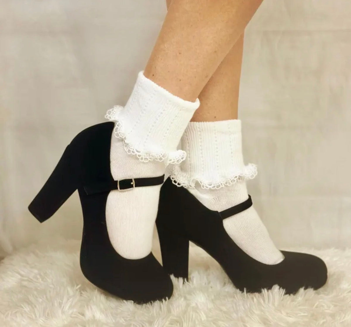 Black high-heeled shoes with white socks featuring lace cuffs on a neutral background