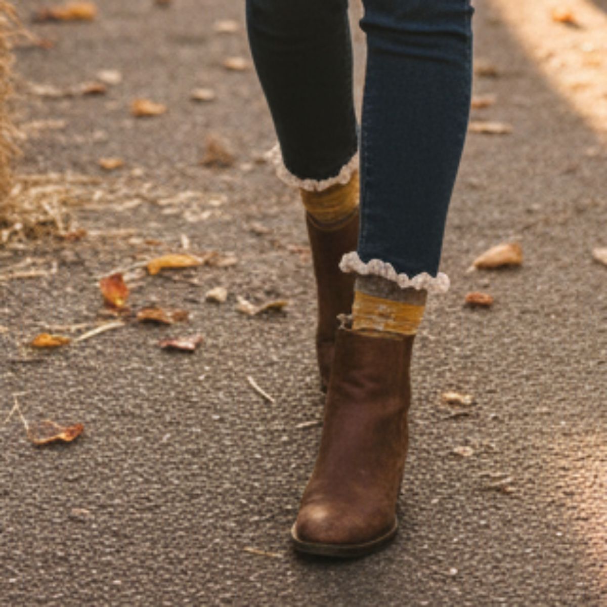 Brown knee-high boots with lace cuffs worn with rolled-up jeans on a road with autumn leaves.