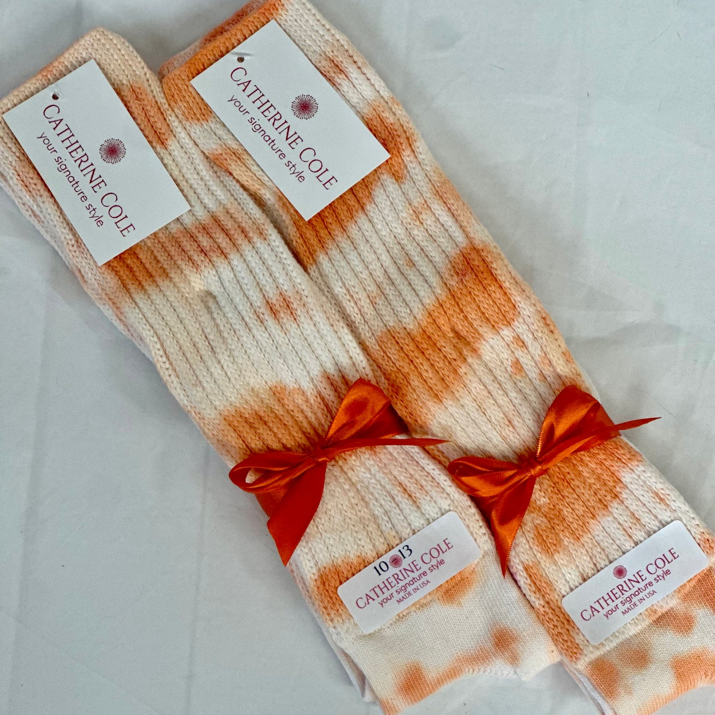 Pair of Catherine Cole tie dye sockssocks with a red ribbon on a light background