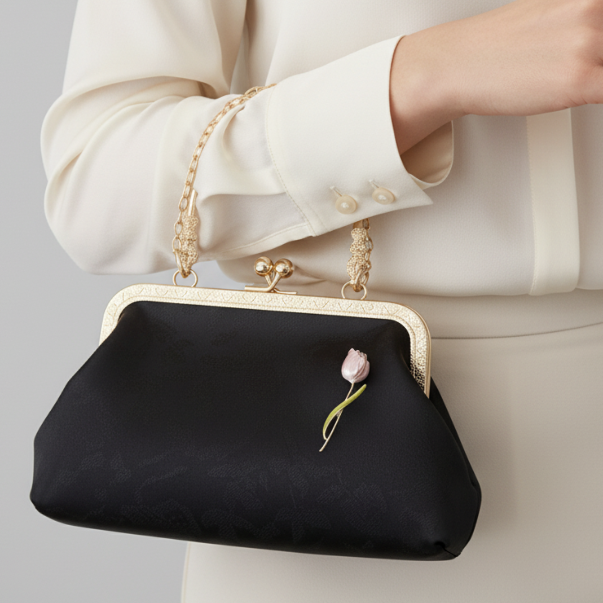 Black clutch bag with gold frame and floral detail held by a person wearing a white outfit.