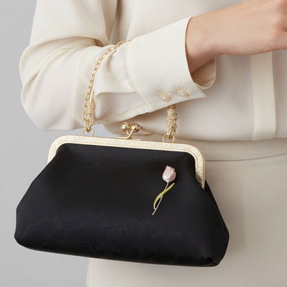 Black clutch bag with gold frame and floral detail held by a person wearing a white outfit.