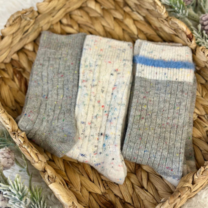 Three pairs of socks in gray, white with speckles, and gray with a blue stripe on a woven basket. Catherine cole