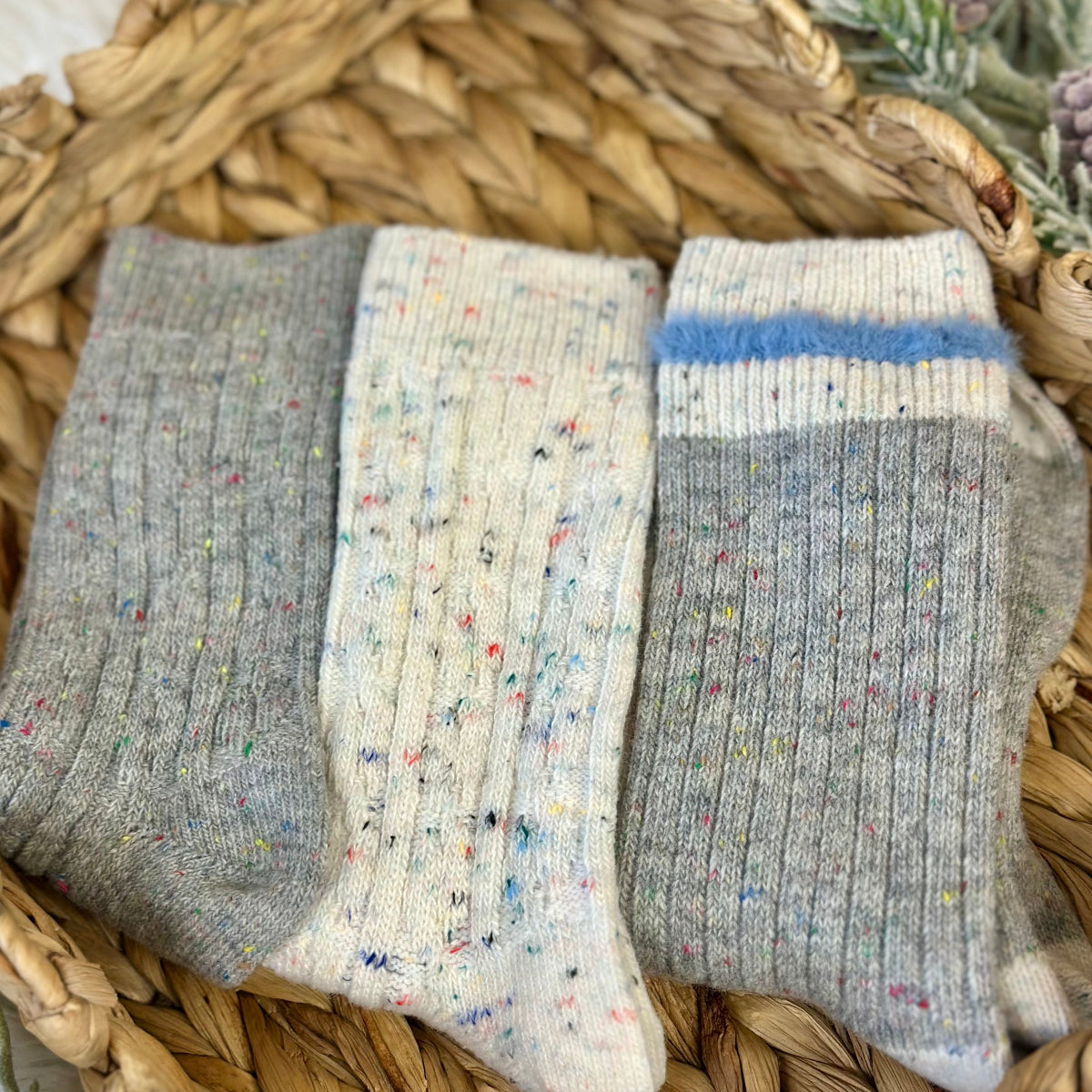 Three pairs of socks in gray, white with multicolor speckles, and blue striped gray on a woven basket background. Cozy grey mix patterned socks - 3 pair gift set + wish bracelet