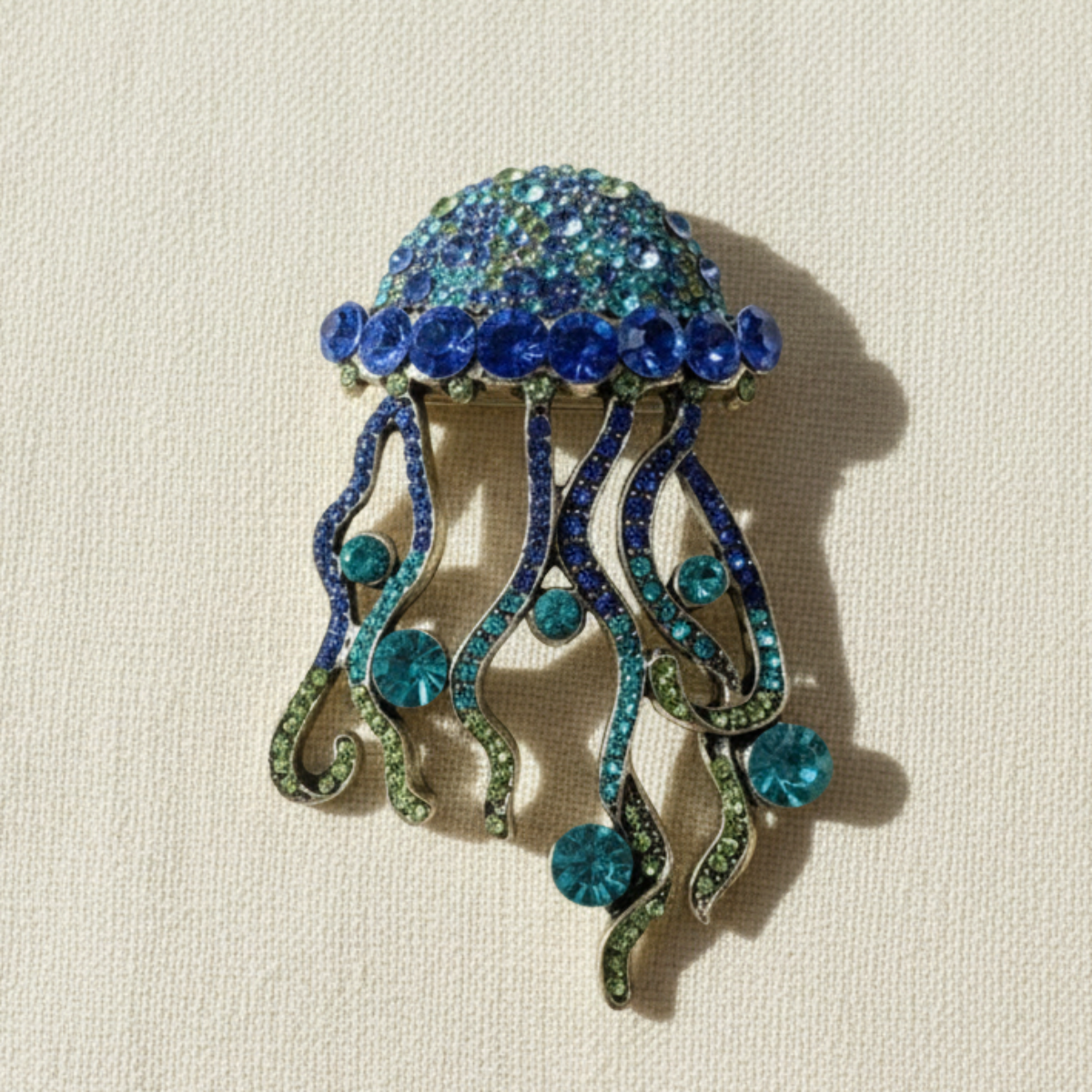 Jellyfish-shaped brooch with blue and green gemstones on a beige background