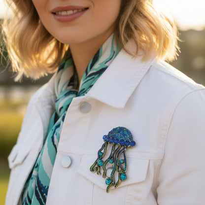Person wearing a white coat with a blue jellyfish brooch and a green scarf. 
