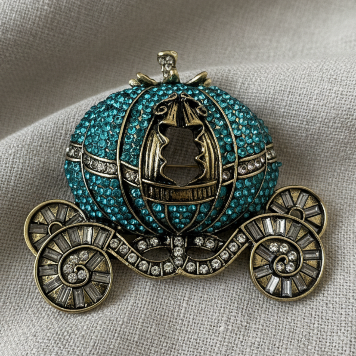 Decorative pumpkin with carriage design, embellished with turquoise stones and gold accents on a textured fabric background. Crystal Pumpkin Coach Brooch Pin - Cinderella's Enchanted Carriage