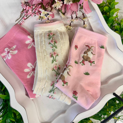 Three pairs of pink and white socks with floral and bunny designs on a decorative plate.