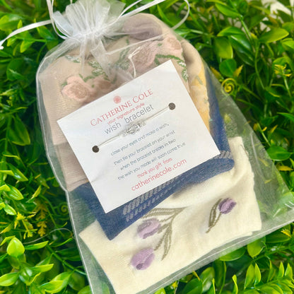 Catherine Cole wish bracelet in clear packaging with a green leafy background