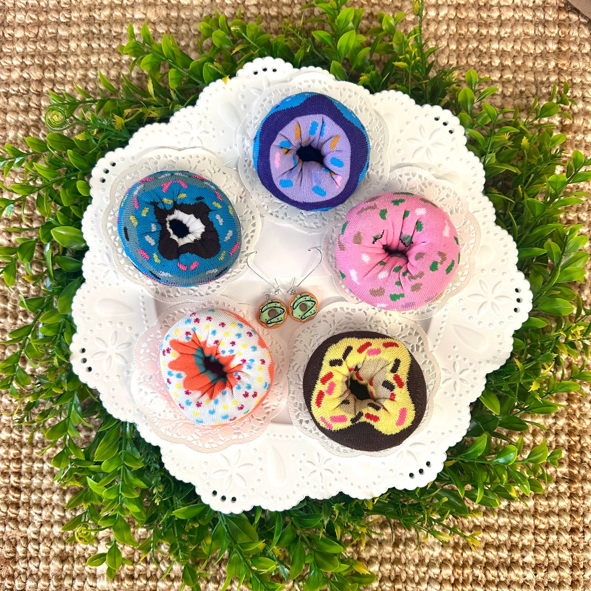 Four colorful doughnut print socks displayed on white lace plate – novelty sock gift set