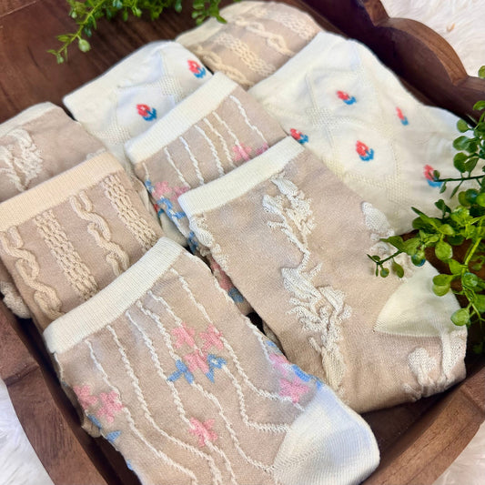 Set of folded beige socks with floral patterns on a wooden surface. Lightweight Summer Ankle Socks 4-Pack Bundle with Wish Bracelet - Women's 6-9 