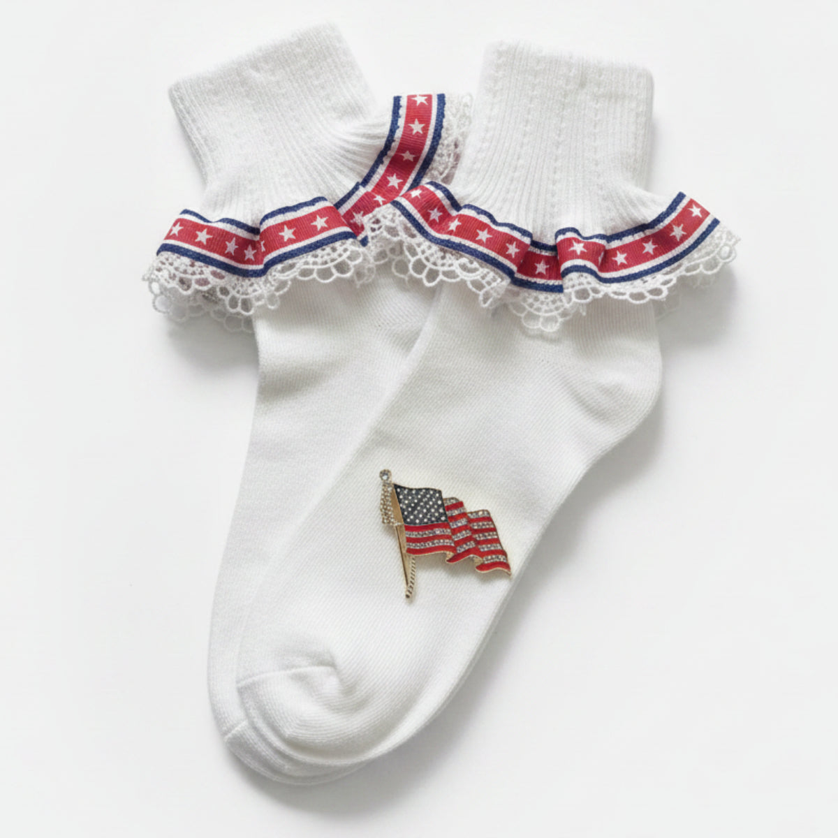 White socks with red, white, and blue trim and an American flag design on a wooden surface.  Patriotic Lace Sock & American Flag Pin Gift Set | Stars & Stripes Cuff Socks
