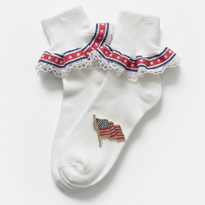 White socks with red, white, and blue trim and an American flag design on a wooden surface.  Patriotic Lace Sock & American Flag Pin Gift Set | Stars & Stripes Cuff Socks