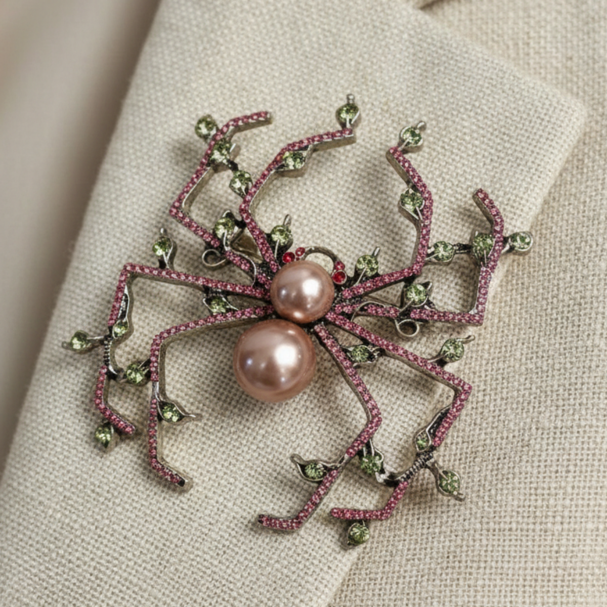 Decorative brooch with pink pearls and green gemstones on a beige fabric background. Pearl & Crystal Spider Brooch Pin - Charlotte's Garden Vintage Jewelry