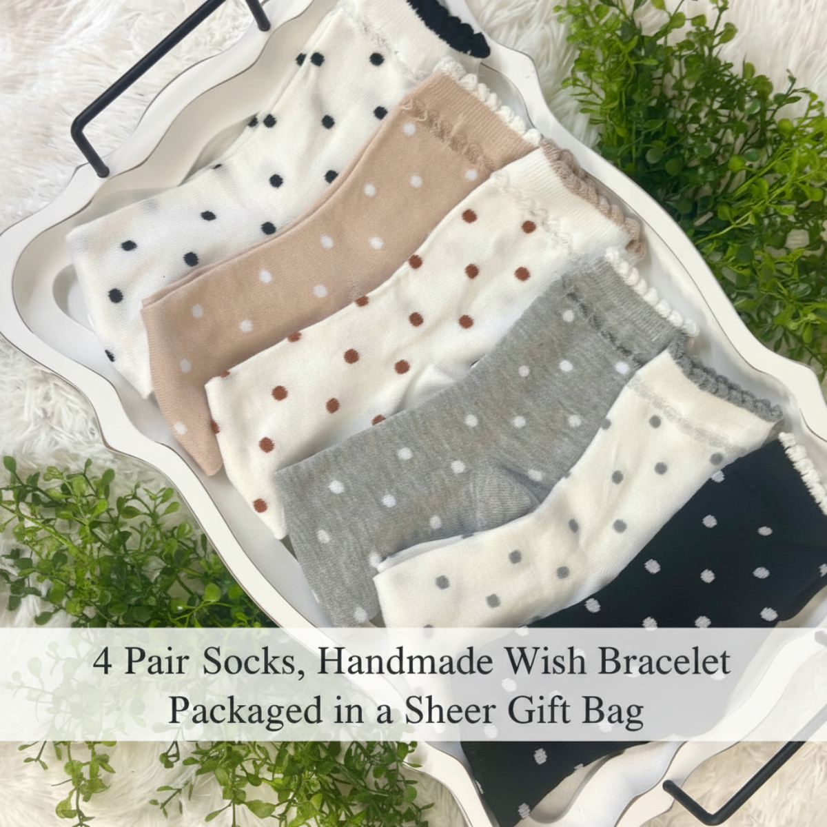 Four pairs of handmade socks in different colors and patterns (black and white polka dots, beige and white polka dots, brown and white polka dots, gray and white polka dots) arranged in a white tray with decorative greenery. A text overlay at the bottom reads '4 Pair Socks, Handmade Wish Bracelet Packaged in a Sheer Gift Bag'.
