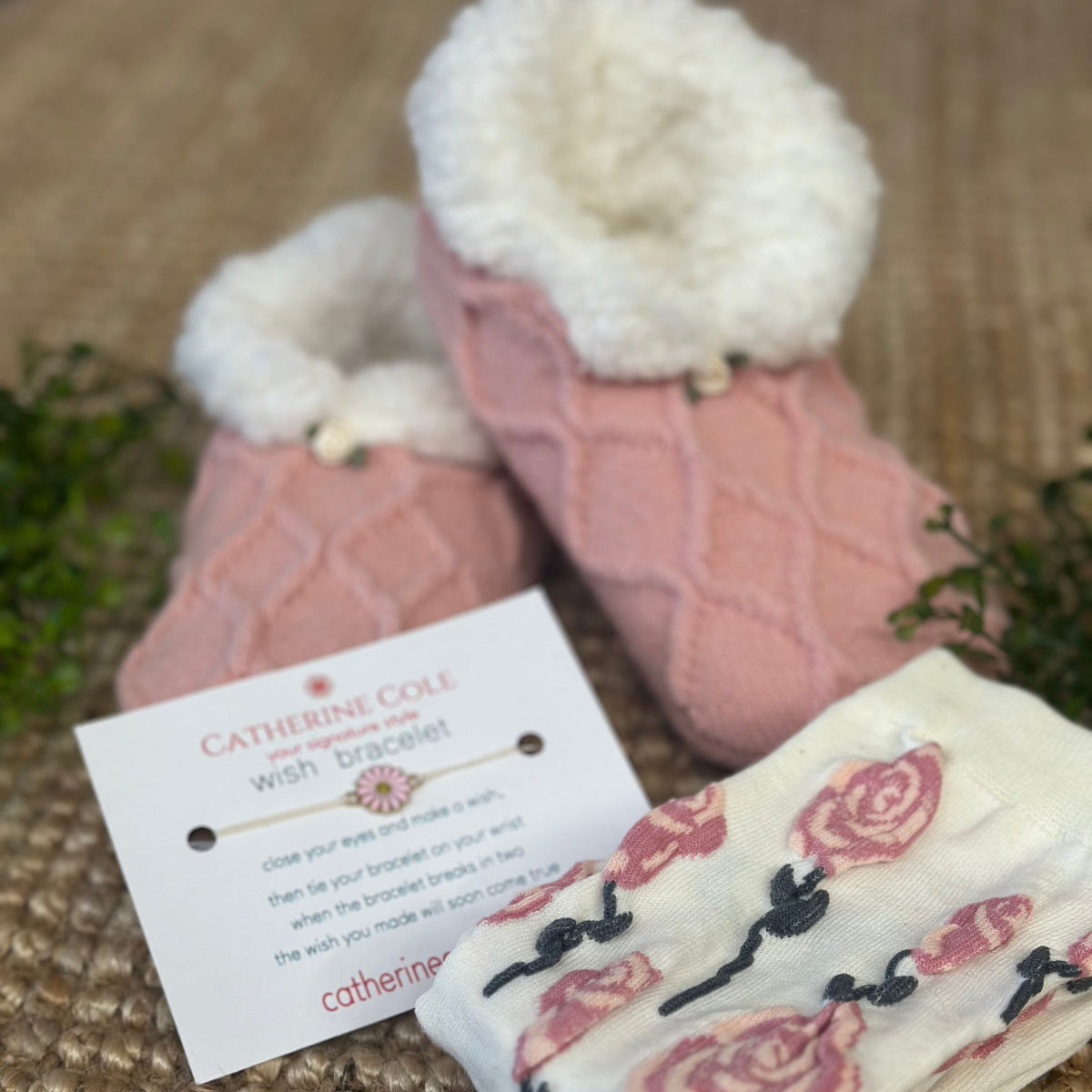 Pink slippers with white fur lining and a matching rose-patterned towel on a textured surface.  
Pretty in Pink Slipper Sock Gift Set - Grip Bottom + Floral Socks + Wish Bracelet
