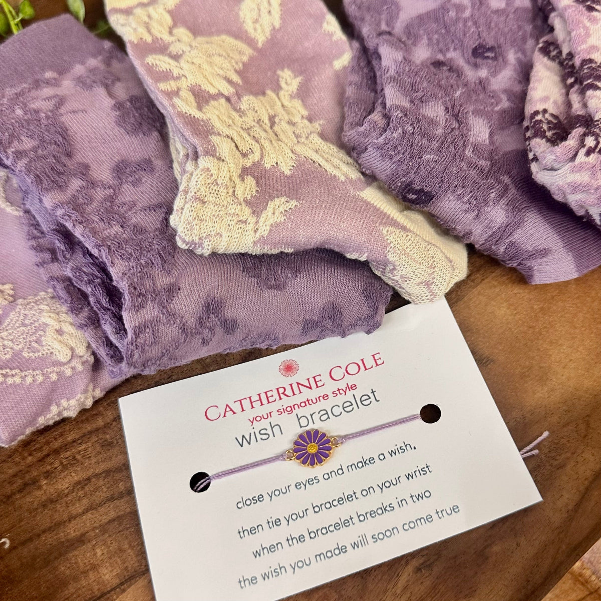 Purple fabric with a 'Catherine Cole' wish bracelet card on a wooden surface