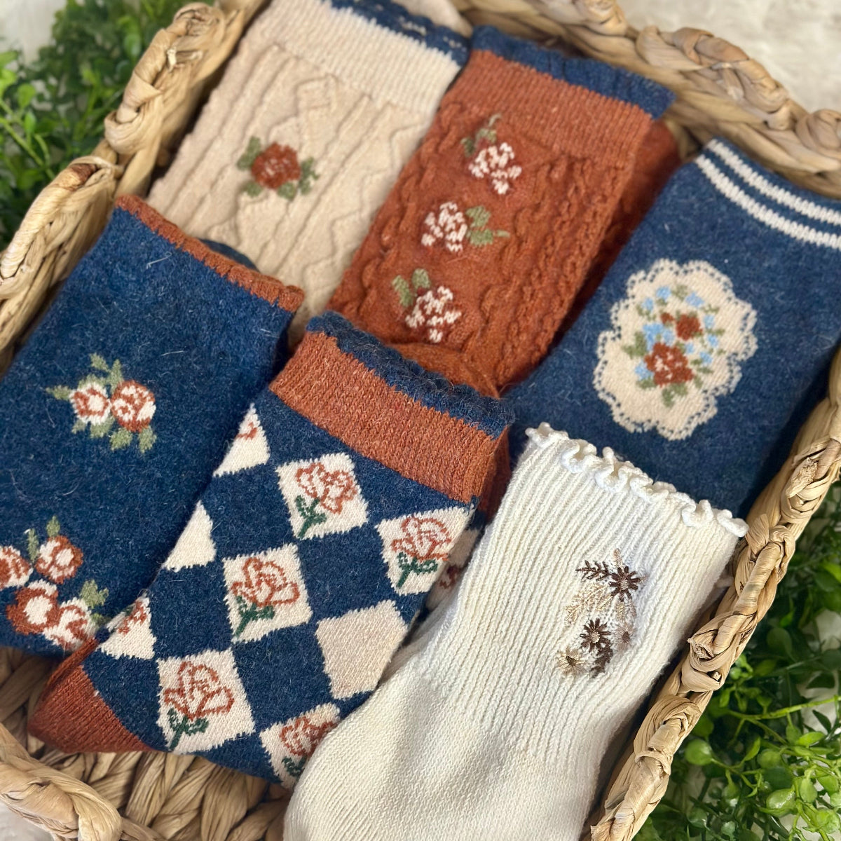 Collection of patterned socks in a woven basket with greenery in the background Catherine cole