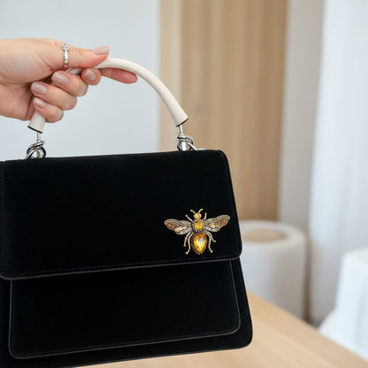 White handbag with a bee emblem on a dark brown background by Catherine Cole