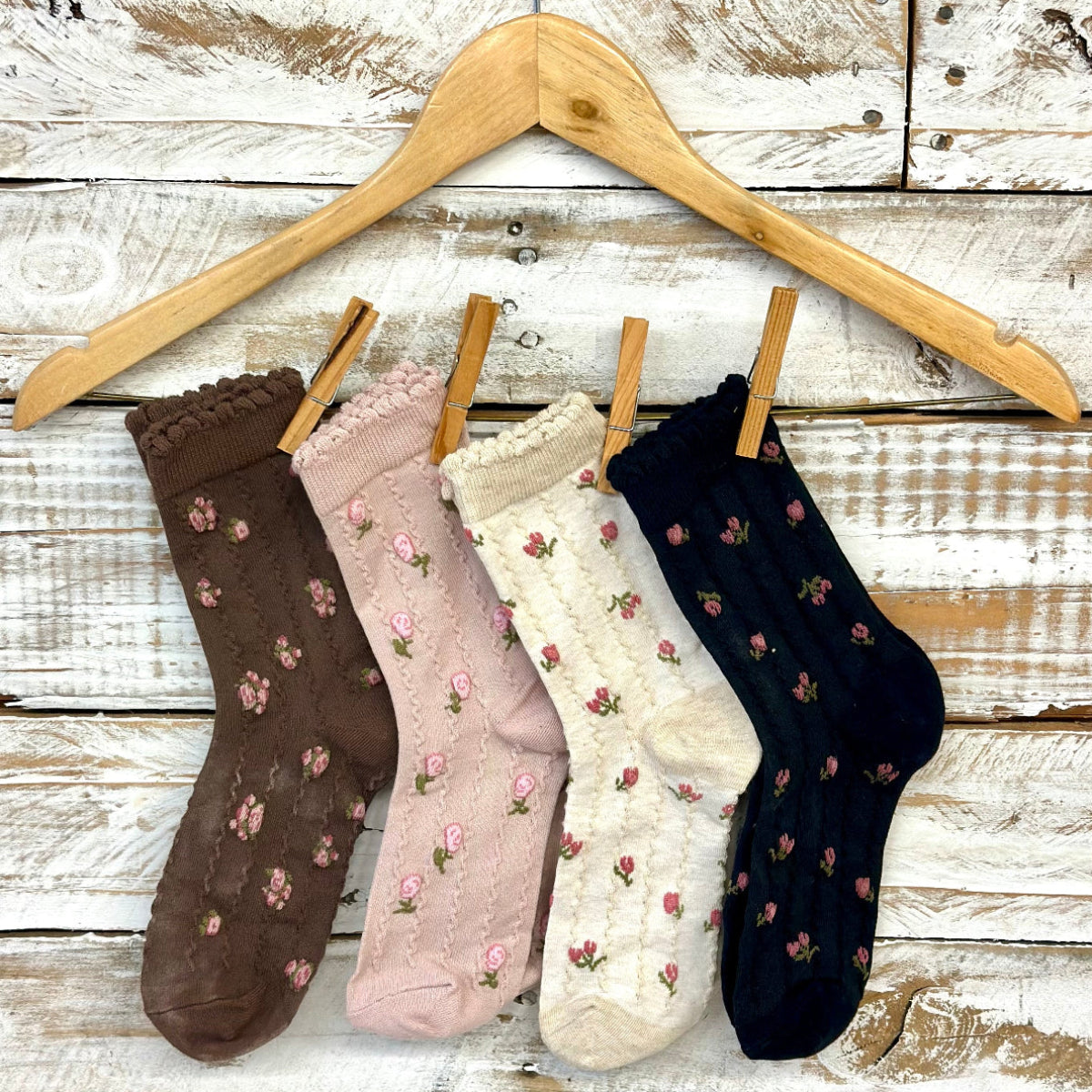 Four pairs of floral-patterned socks hanging on a wooden hanger against a rustic wooden background.