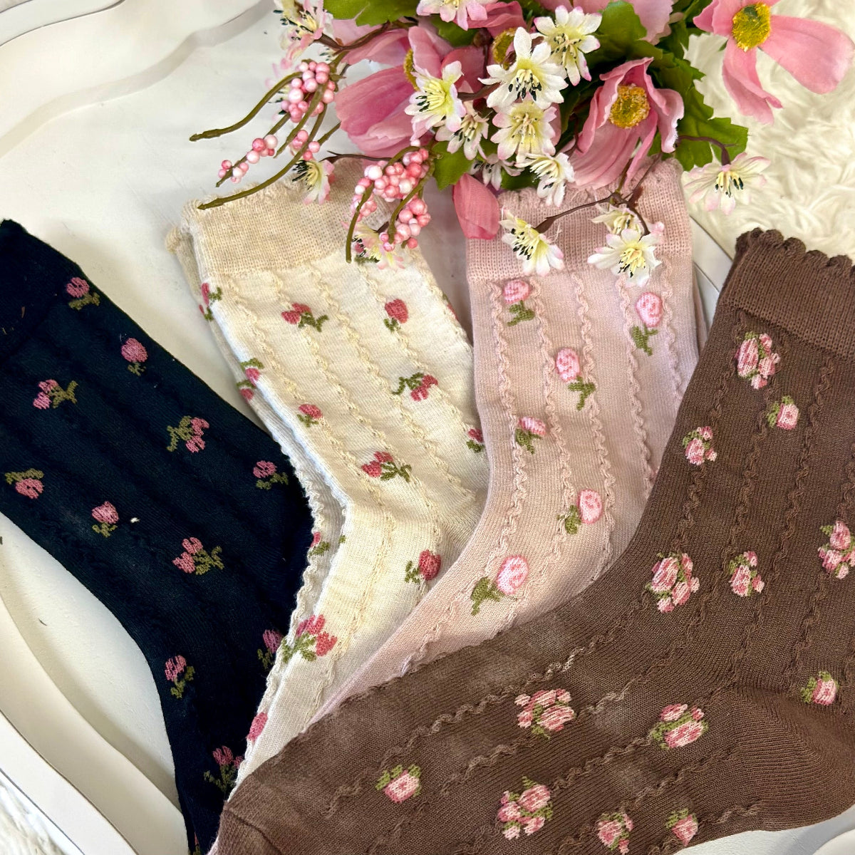 Three pairs of floral-patterned socks in black, white, and brown on a white surface with flowers.