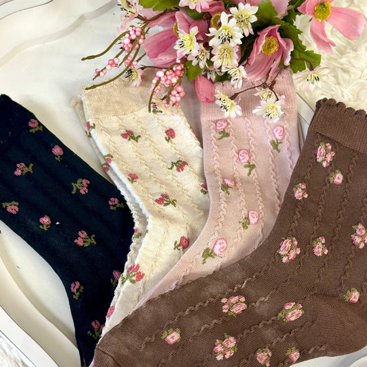 Three pairs of floral-patterned socks in black, white, and brown on a white surface with flowers.