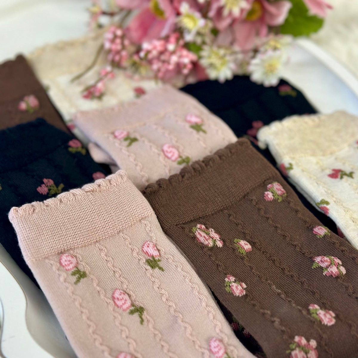 Set of embroidered socks with floral patterns on a white plate with flowers in the background. Catherine cole