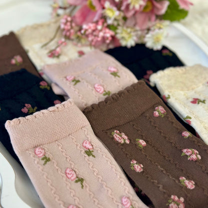 Set of embroidered socks with floral patterns on a white plate with flowers in the background. Catherine cole