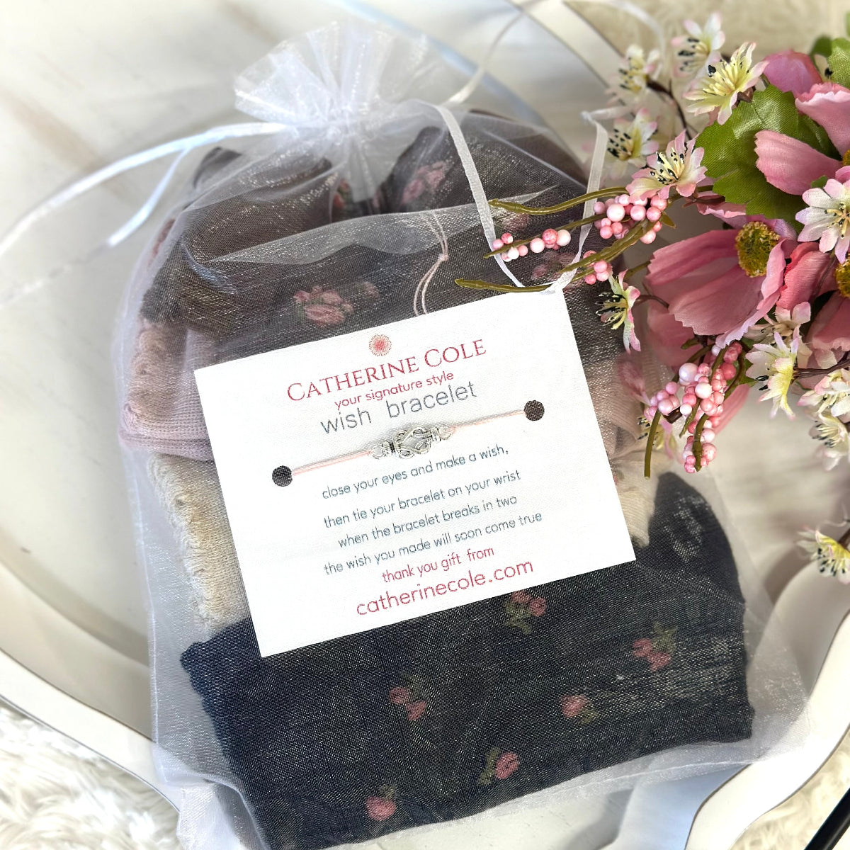 Catherine Cole wish bracelet in a clear bag with a tag and flowers on a white surface