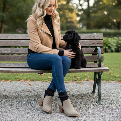 Beige ankle boots with brown block heels worn with blue jeans on a gravel surface.
