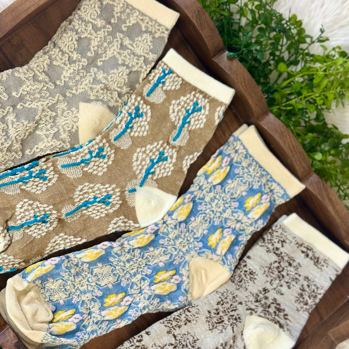 Set of patterned socks displayed in a wooden box with a plant in the background.  Spring Floral Ankle Socks 4-Pack Bundle with Wish Bracelet - Women's 6-9
