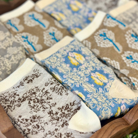 Set of patterned socks with floral and abstract designs on a wooden surface.  Spring Floral Ankle Socks 4-Pack Bundle with Wish Bracelet - Women's 6-9