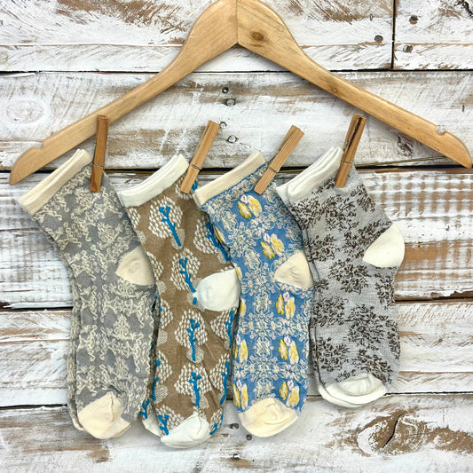 Four pairs of patterned socks hanging on a wooden hanger against a rustic wooden background.  Spring Floral Ankle Socks 4-Pack Bundle with Wish Bracelet - Women's 6-9