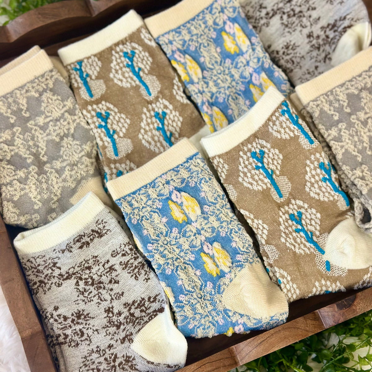 Set of patterned socks on a wooden surface with a natural background. Spring Floral Ankle Socks 4-Pack Bundle with Wish Bracelet - Women's 6-9