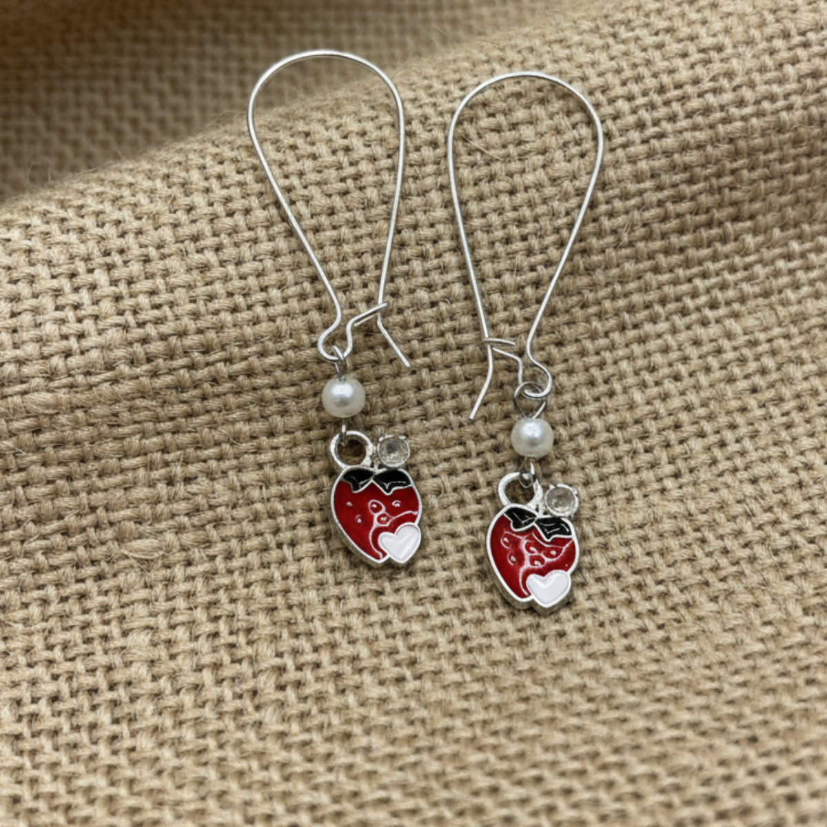 Pair of earrings with red heart-shaped charms on a textured beige fabric background
