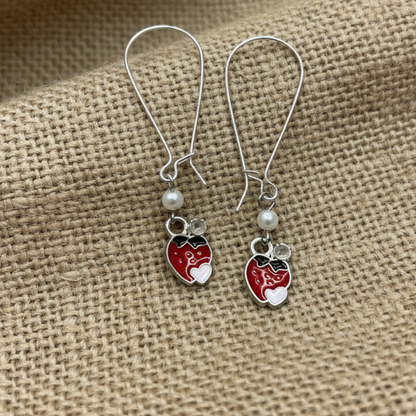 Pair of earrings with red heart-shaped charms on a textured beige fabric background