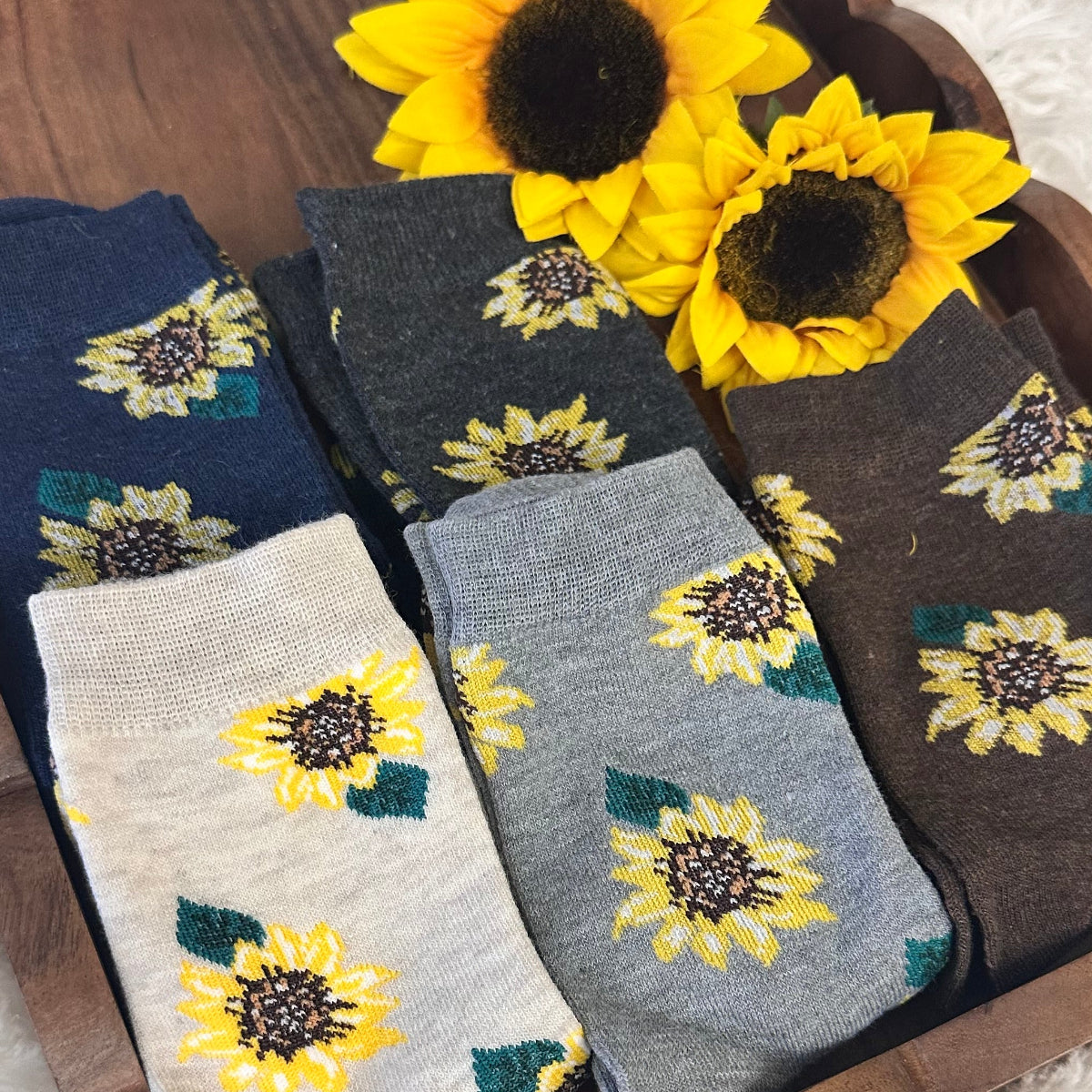 Set of sunflower-patterned socks on a wooden tray with sunflowers beside them.  Sunflower Patterned Ankle Socks 5-Pack Bundle with Wish Bracelet - Women's 