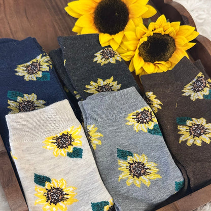 Set of sunflower-patterned socks on a wooden tray with sunflowers beside them.  Sunflower Patterned Ankle Socks 5-Pack Bundle with Wish Bracelet - Women's 