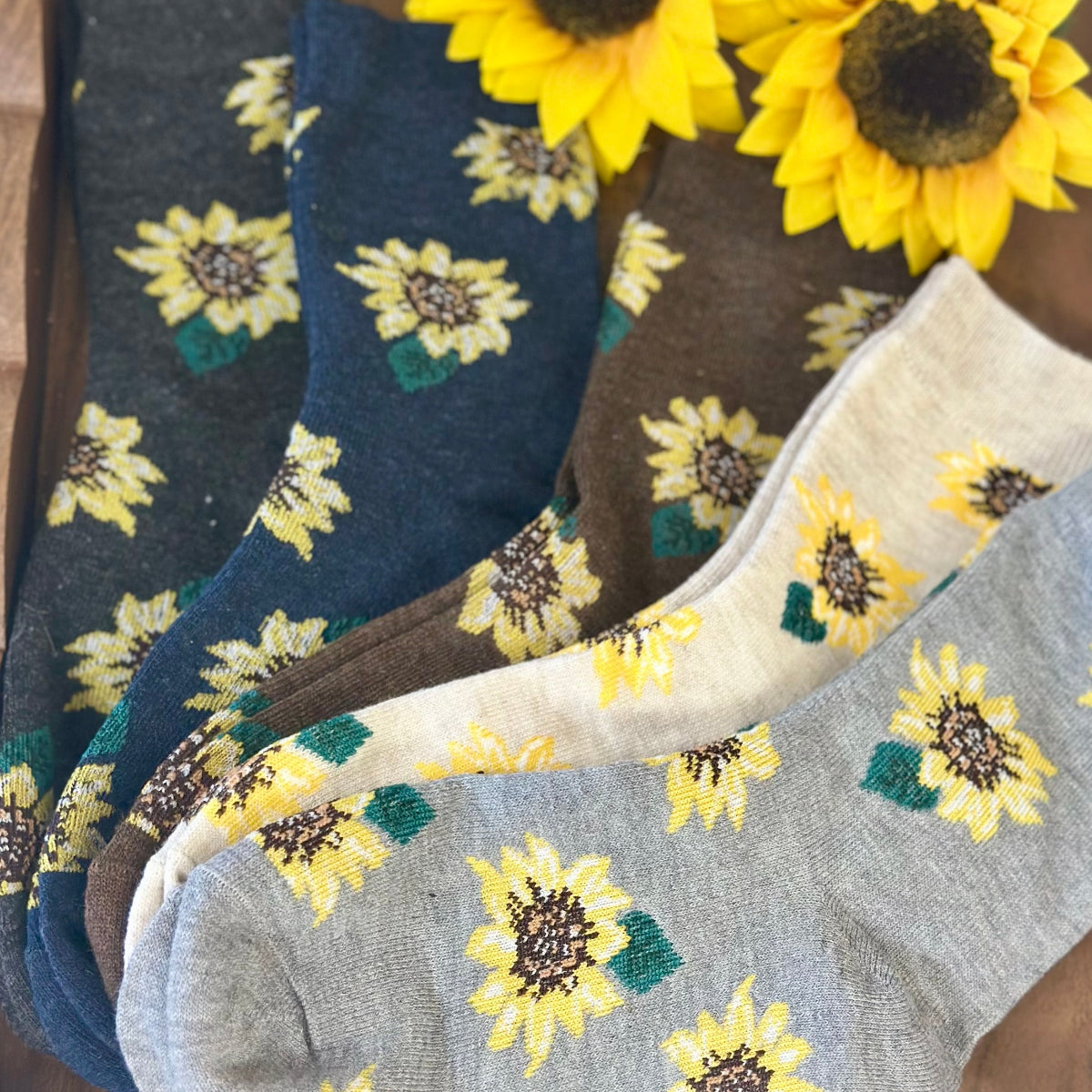 Sunflower-patterned socks in various colors on a wooden surface with sunflowers.  Sunflower Patterned Ankle Socks 5-Pack Bundle with Wish Bracelet - Women's 