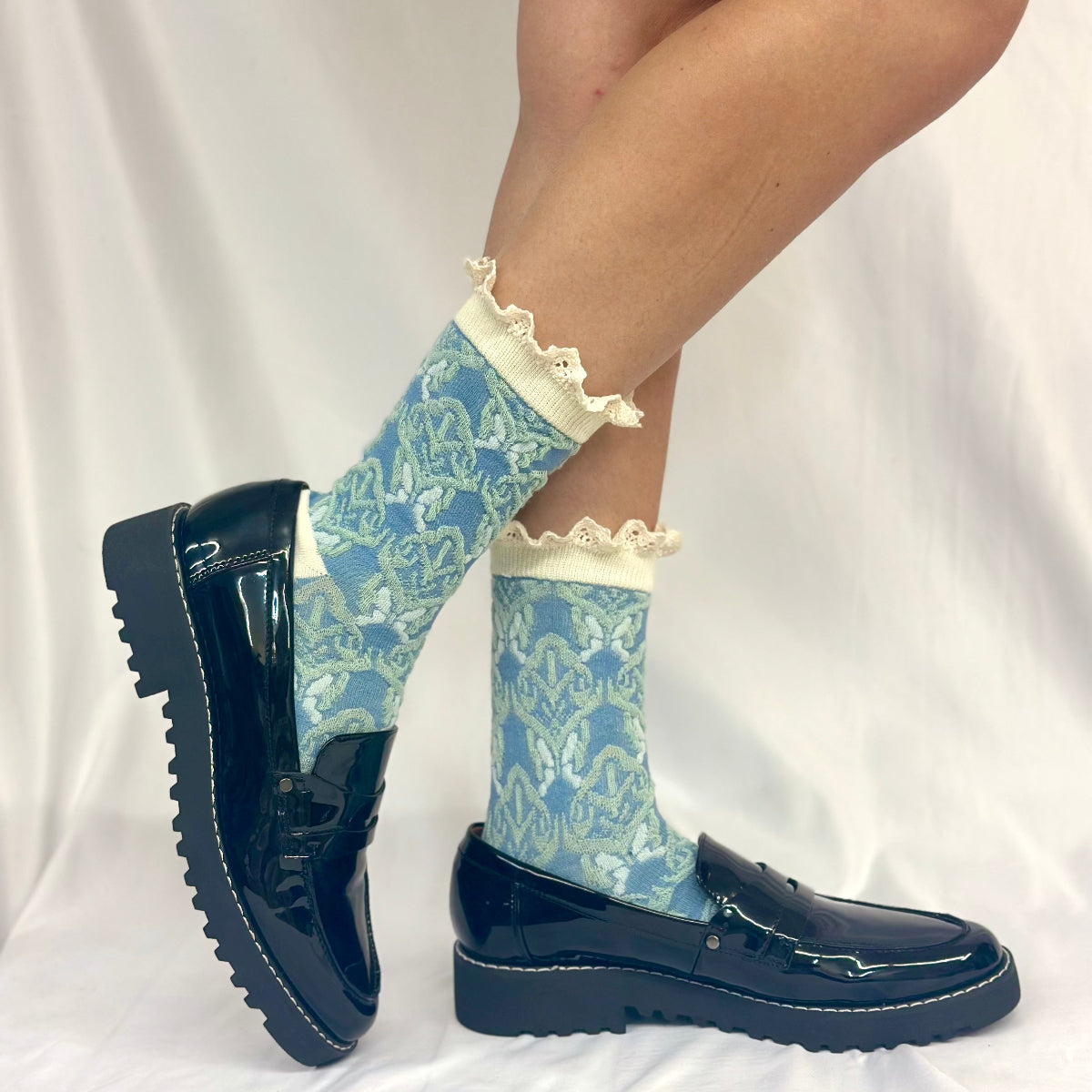 Blue patterned socks with lace trim worn with black shoes on a white background. TAPESTRY  print lace top ankle sock - blue