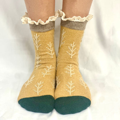 Mustard yellow socks with white floral patterns and green toes worn by a person on a white background - TWIGS  lace topped socks - mustard