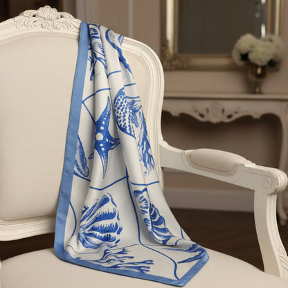 Blue and white patterned towel draped over a white chair in a decorative setting.  The Amalfi | Ocean Silk-Look Square Scarf 25"
