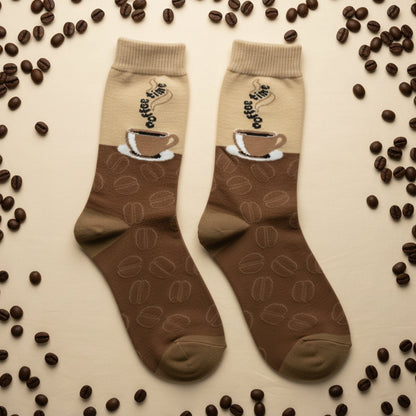 Pair of brown socks with coffee cup design on a beige background with scattered coffee beans.  The Coffee Lover Gift Set (2-Pack Socks + Coffee Cup Earrings)
