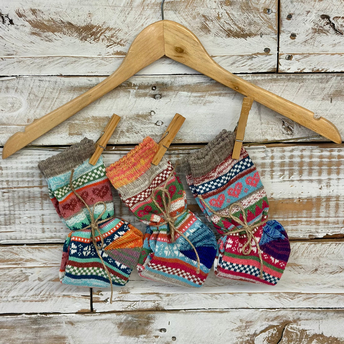 Colorful knitted socks hanging on a wooden hanger against a rustic wooden background, Valentine_s_Heart_Socks_Gift_Set_-_3_Pairs_with_Wish_Bracelet