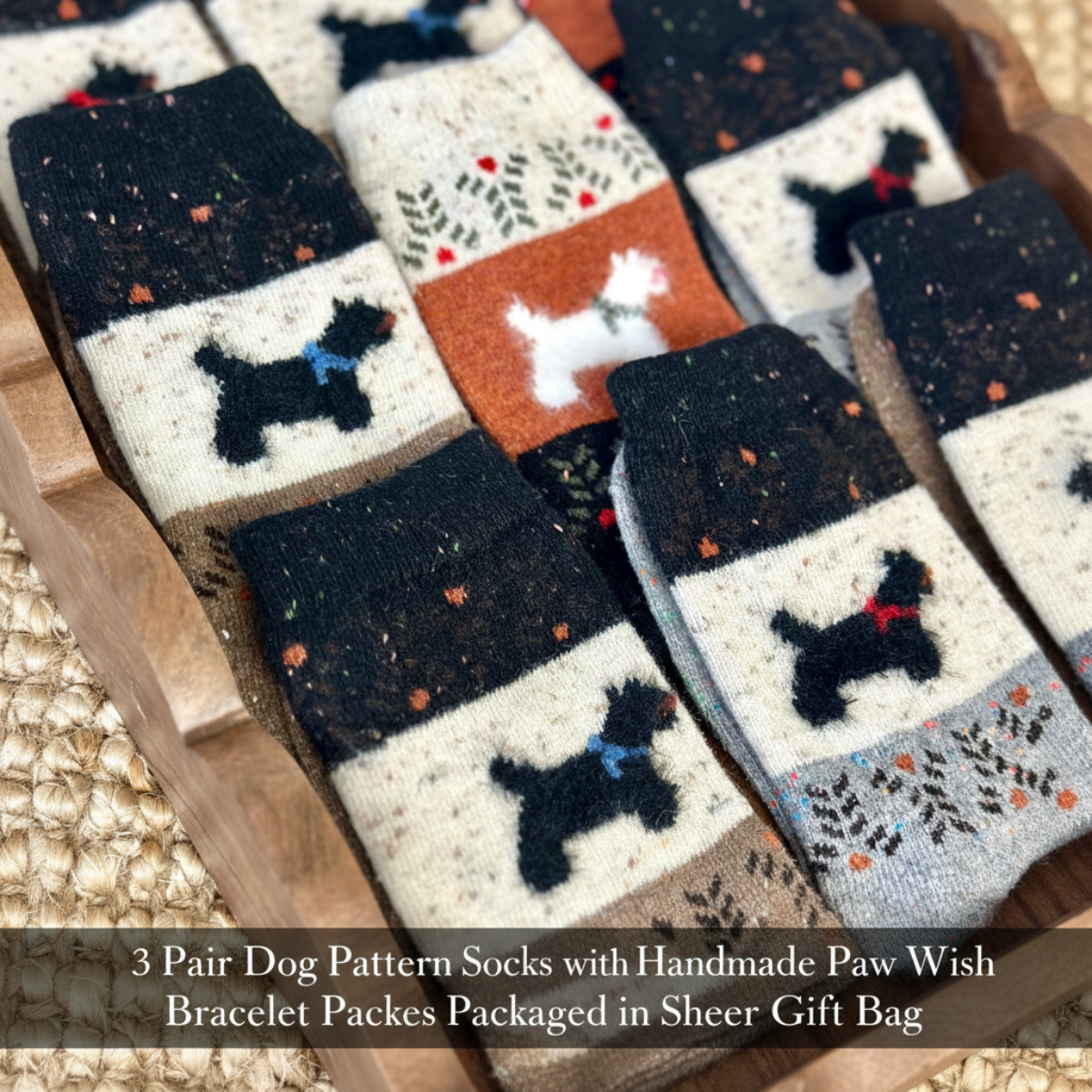 Three pairs of handmade dog-pattern socks displayed in a wooden tray, featuring black dog silhouettes on cream and orange sections, with paw print and floral details. Text overlay at the bottom reads: '3 Pair Dog Pattern Socks with Handmade Paw Wish Bracelet Packs Packaged in Sheer Gift Bag'.