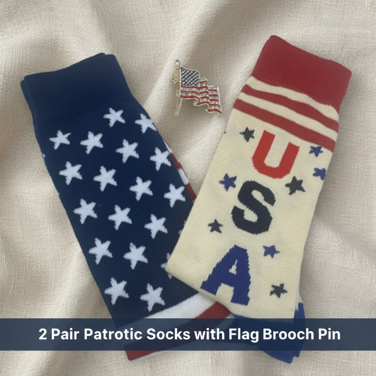 Two patriotic socks displayed on a cream fabric background, one navy blue with white stars and one cream with red and navy lettering and stars. A small American flag brooch pin is placed above them.