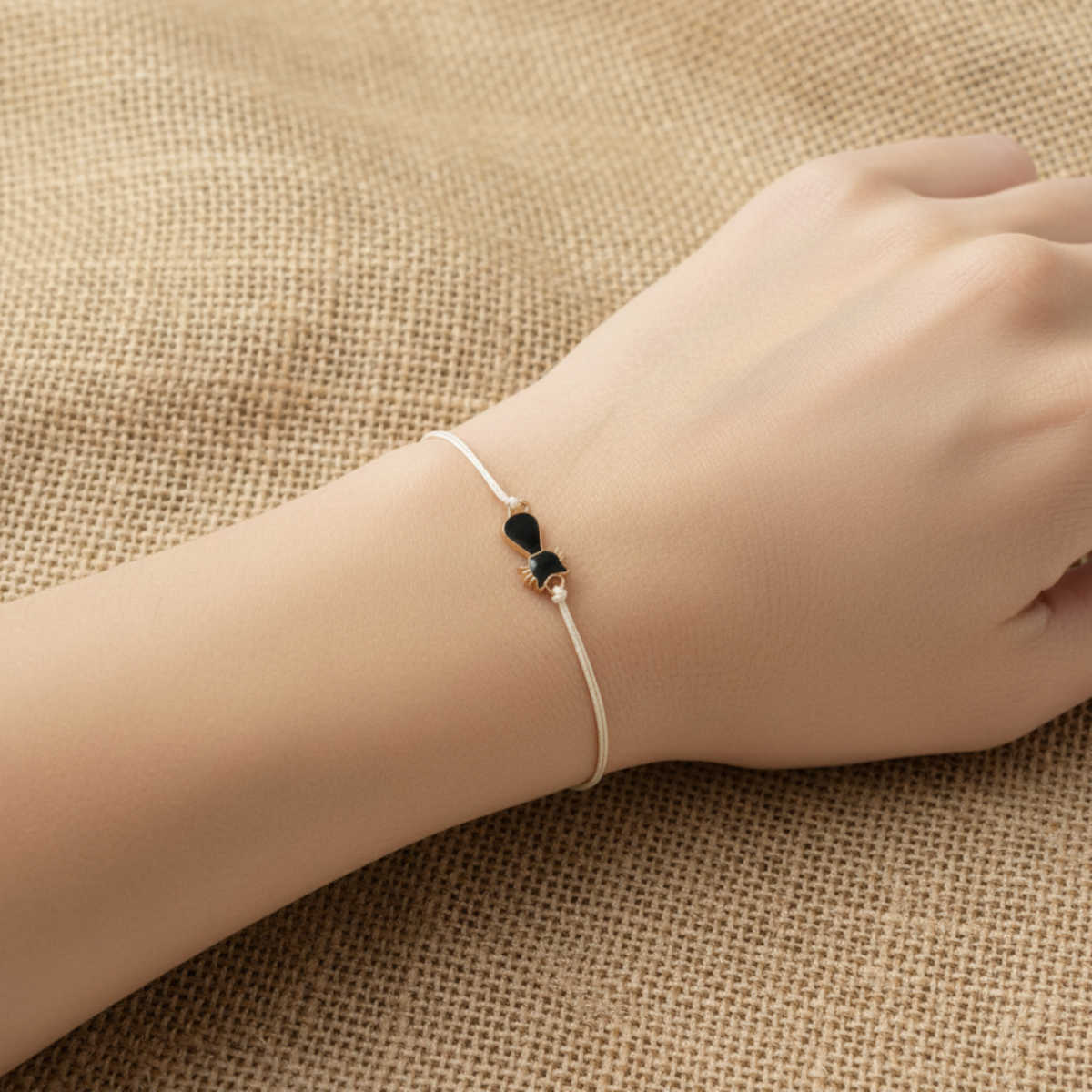 Hand wearing a delicate bracelet with a black heart charm on a textured beige background