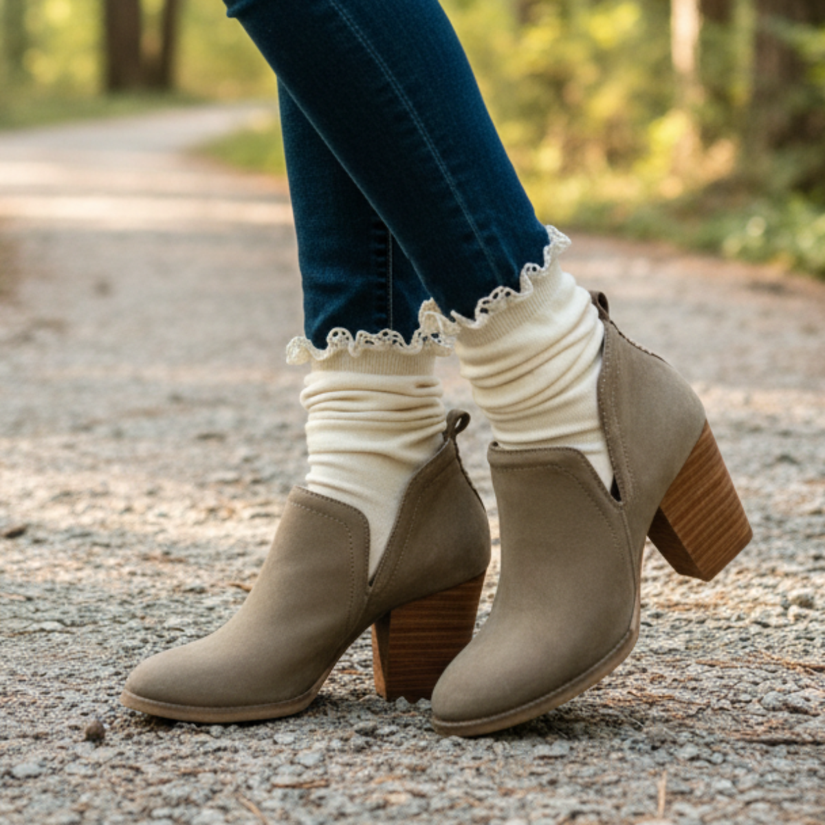 Beige ankle boots with brown soles worn with blue jeans and white socks on a gravel path.